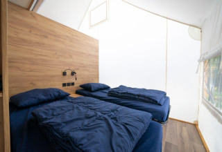 Foto interior de una tienda safari con dos camas individuales, panel de madera y ventana lateral.