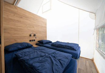 Interior photo of a safari tent bedroom with two single beds, wood paneling, and a side window.