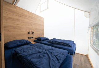 Interior photo of a safari tent bedroom with two single beds, wood paneling, and a side window.