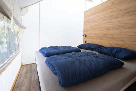 Innenansicht eines Safarizelts mit Doppelbett, blauen Decken und einem hölzernen Kopfteil.