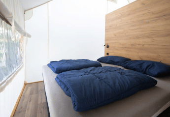 Innenansicht eines Safarizelts mit Doppelbett, blauen Decken und einem hölzernen Kopfteil.