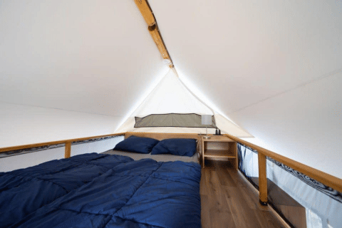 Intérieur d'une tente safari avec lit double, linge de lit bleu, plancher en bois et table de chevet.