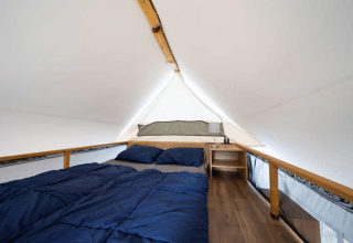 Vista interna di una tenda safari con letto matrimoniale, biancheria blu e comodino con lampada.