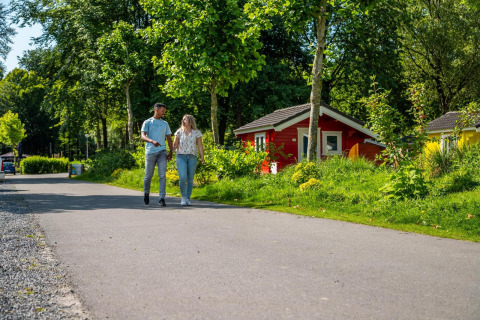 Una pareja joven camina de la mano junto a coloridas cabañas de glamping rodeadas de vegetación y árboles.