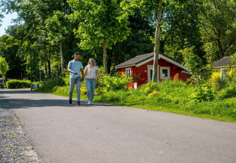 A young couple strolls hand in hand past colorful glamping cabins surrounded by lush greenery and trees.