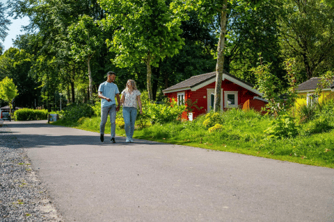 Una giovane coppia passeggia mano nella mano accanto a colorate cabine glamping tra alberi e vegetazione.