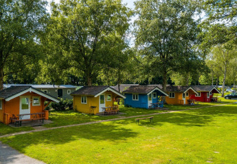Bungalow in legno colorati su un campeggio verde sotto grandi alberi, ideale per un'esperienza glamping.
