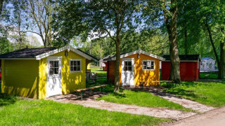 To farverige hytter i træ blandt grønne træer på en solrig dag ved Cabin lodge, fredfyldt omgivelser.
