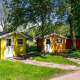To farverige hytter i træ blandt grønne træer på en solrig dag ved Cabin lodge, fredfyldt omgivelser.
