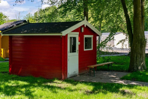 Cabaña de madera roja con puerta blanca y banco, situada en el Het Amsterdamse Bos, Países Bajos.