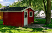 Rood houten huisje met witte deur en bank ervoor, gelegen in Het Amsterdamse Bos, Nederland.