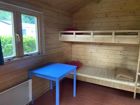 Interior de una cabaña de madera con literas, mesa azul y ventana en Cabin at Het Amsterdamse Bos, Países Bajos.
