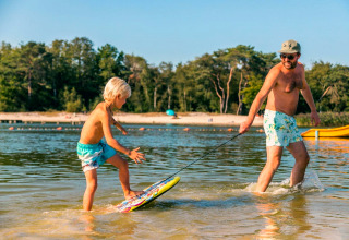 Un homme tire un enfant sur un skimboard dans l'eau peu profonde lors de vacances en glamping.
