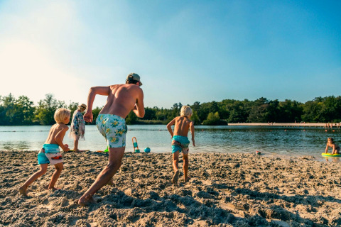 Famille profitant d'une journée ensoleillée à la plage lors d'un séjour glamping, enfants courant vers l'eau.