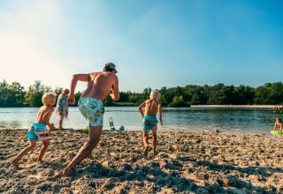 Famille profitant d'une journée ensoleillée à la plage lors d'un séjour glamping, enfants courant vers l'eau.