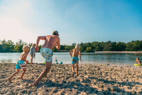 Familie genießt einen sonnigen Tag am Strand eines Glamping-Resorts, Kinder laufen zum Wasser.