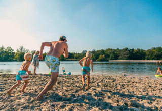 Gezin beleeft een zonnige dag aan het strand op een glamping, terwijl kinderen naar het water rennen.