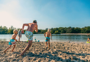 Famiglia si gode una giornata di sole in spiaggia presso una sistemazione glamping, bambini corrono all'acqua.