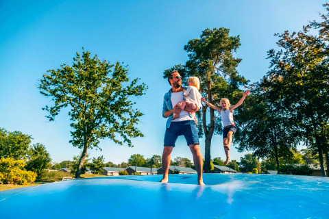 Famille s'amusant sur un grand coussin gonflable en plein air lors d'un séjour en glamping ensoleillé.