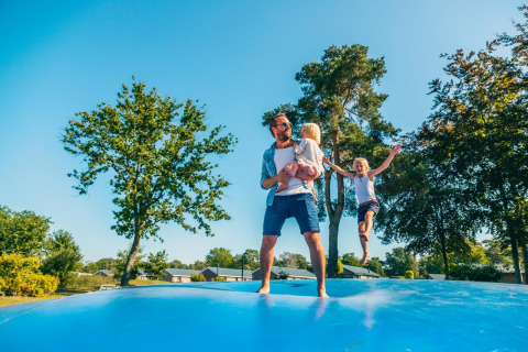Gezin speelt samen op een groot springkussen tijdens hun zonnige glampingverblijf in het groen.