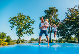 Familia divirtiéndose en un gran cojín hinchable bajo el sol durante una estancia de glamping.
