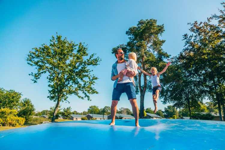 Familie genießt gemeinsam eine große Hüpfburg bei sonnigem Wetter auf einem Glampingplatz.