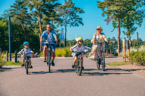 Une famille de quatre personnes fait une balade à vélo sous le soleil dans un site de glamping verdoyant.