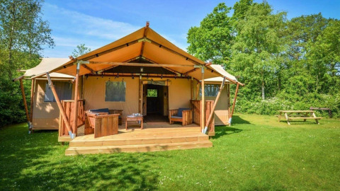 Hébergement glamping avec tente toilée, terrasse en bois, assises extérieures et espace vert arboré.
