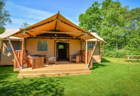 Alloggio glamping con tenda, veranda in legno, aree relax esterne e circondato da verde e alberi.
