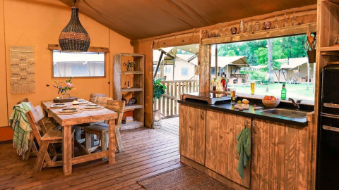 Hébergement glamping chaleureux avec meubles en bois rustique, table à manger et cuisine ouverte sur la nature.