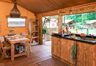 Hébergement glamping chaleureux avec meubles en bois rustique, table à manger et cuisine ouverte sur la nature.