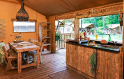 Hyggelig glamping-indkvartering med træmøbler, spisebord og åbent køkken med udsigt til naturen.