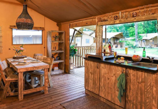 Gezellige glampingaccommodatie met houten meubels, eettafel en open keuken met zicht op de natuur.