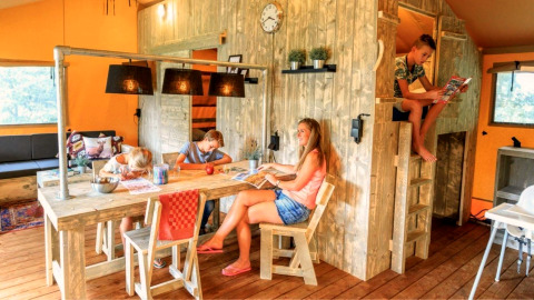 Famille profitant de moments ensemble dans un hébergement glamping chaleureux avec meubles en bois.