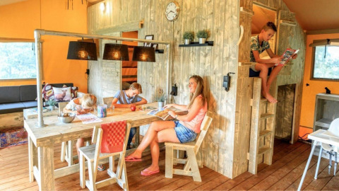 Famille profitant de moments ensemble dans un hébergement glamping chaleureux avec meubles en bois.