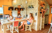Familie nyder tid sammen i et hyggeligt glamping-indkvartering med træmøbler og varme farver.