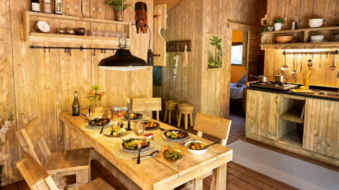 Cabane de glamping rustique avec cuisine en bois, table dressée pour quatre et ambiance chaleureuse.