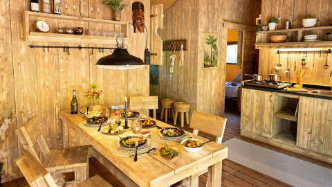 Cabane de glamping rustique avec cuisine en bois, table dressée pour quatre et ambiance chaleureuse.