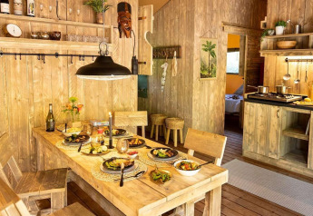 Cabaña de glamping rústica con cocina y mesa de comedor de madera servida para cuatro personas.