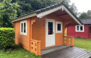 Lille træhytte med terrasse i Het Amsterdamse Bos, Holland, omgivet af grønne træer og græs.