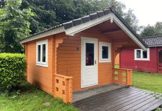 Kleine houten blokhut met terras in Het Amsterdamse Bos, Nederland, omgeven door groen en bomen.