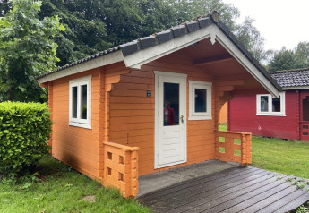 Lille træhytte med terrasse i Het Amsterdamse Bos, Holland, omgivet af grønne træer og græs.