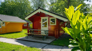 Cabañas glamping rojas y amarillas con porche y bancos, rodeadas de naturaleza verde y soleada.