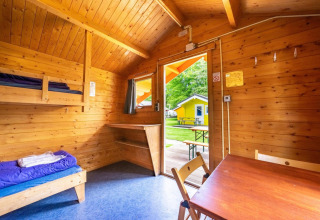 Interior de una cabaña glamping con paredes de madera, literas y vista hacia una cabaña amarilla en el exterior.