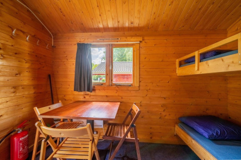 Interior acogedor de cabaña de madera con literas, mesa, sillas y ventana para experiencia glamping.