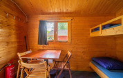 Interior acogedor de cabaña de madera con literas, mesa, sillas y ventana para experiencia glamping.