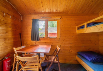 Interno di accogliente cabina in legno con letti a castello, tavolo, sedie e finestra per il glamping.