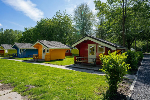 Farverige hytter ved Cabin at Het Amsterdamse Bos i Holland, omgivet af grønne træer og græsplæner.
