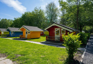 Kleurrijke chalets bij Cabin at Het Amsterdamse Bos in Nederland, omringd door bomen en groene gazons.