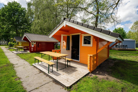 Kleurrijke houten hutten in Het Amsterdamse Bos, Nederland, met picknicktafels en groene omgeving.